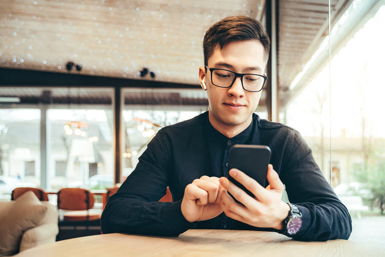 Man wearing glasses, sitting at table, looking at his cell phone