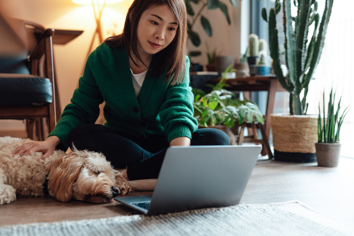 Women sitting on the floor with her dog, look at her laptop