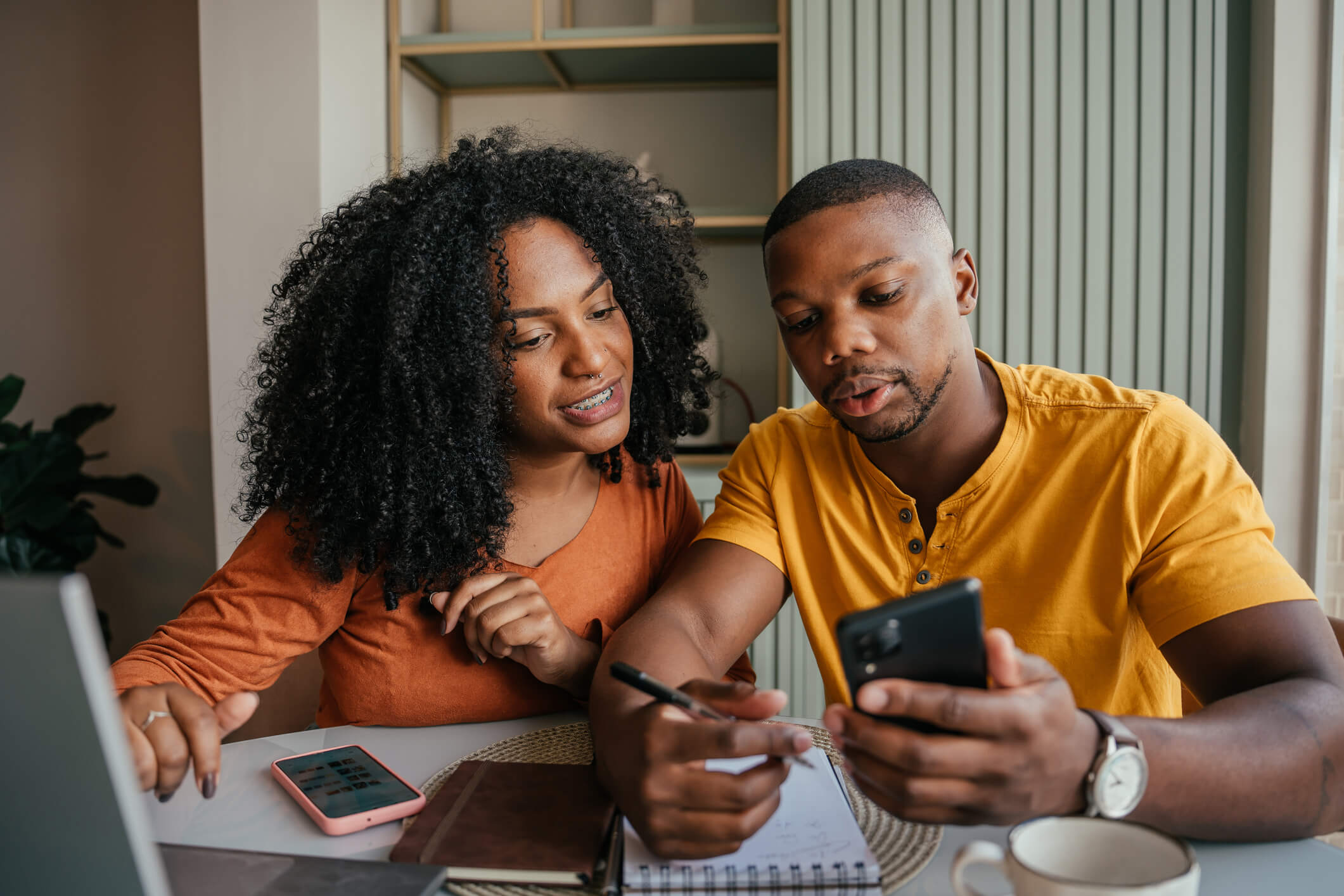 Couple sitting at a table with a notebook, looking at a cell phone