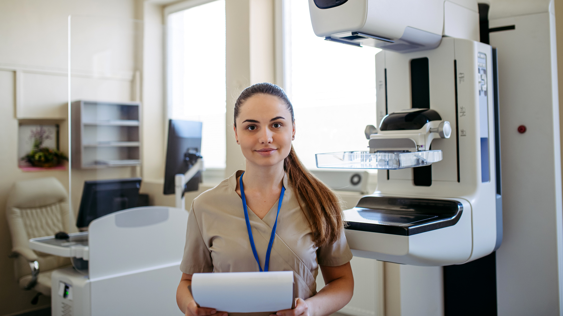 Female lab technician standing in front of a mammogram screening machine
