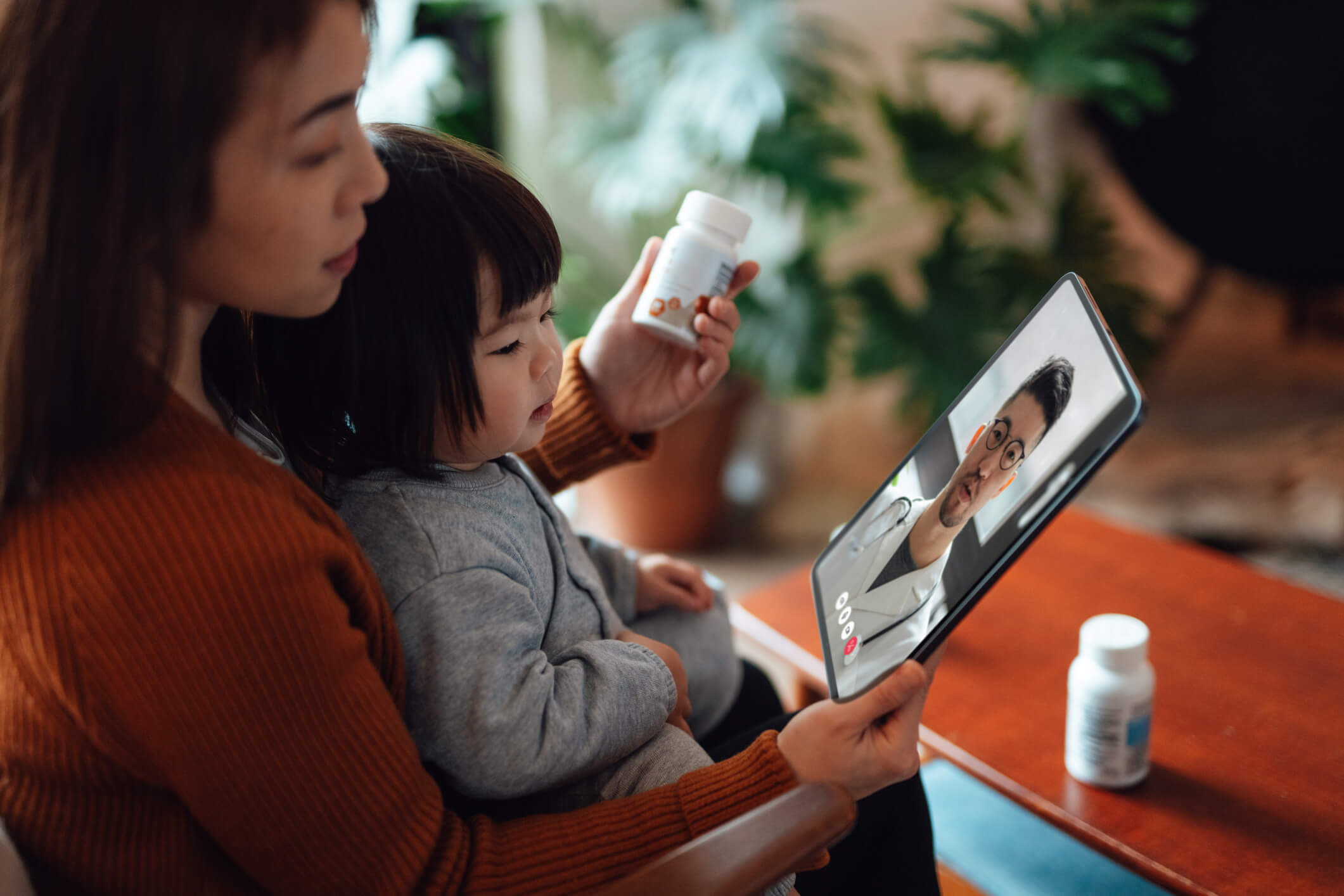 A Mother Video Chatting With Her Health Care Provider About a Prescription She's Holding