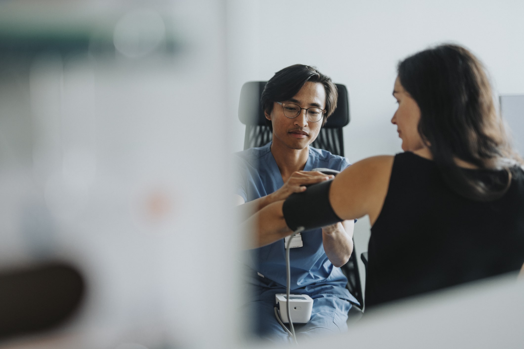 Male medical worker checking blood pressure of female patient during visit at hospital