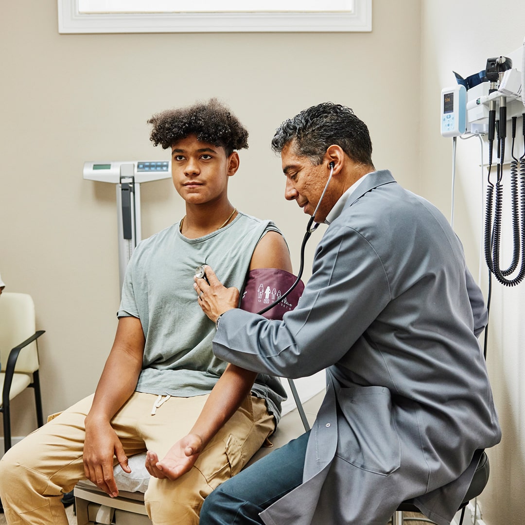 Doctor listening to a patients heart with a stethoscope in an exam room