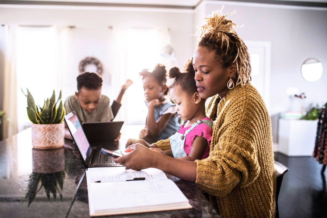 A woman and 3 children sitting at a table with a computer and notebook open