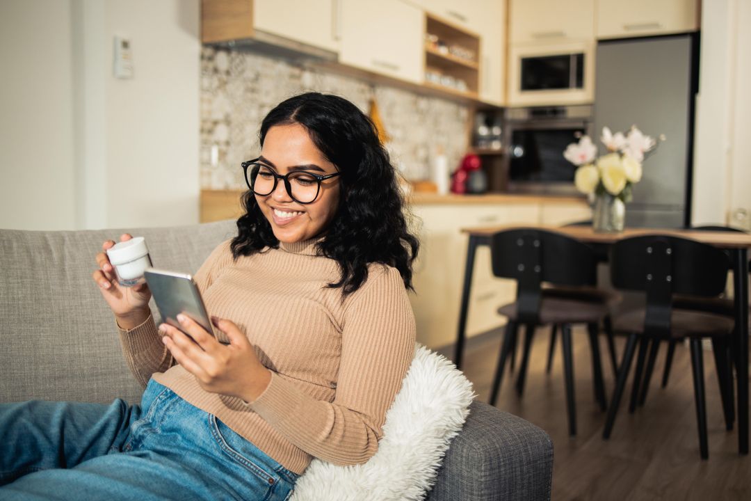 Woman sitting on the couch, holding a container in one hard, and her phone in the other