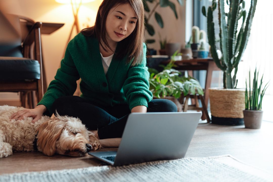 Woman sitting on the floor next to a dog, looking at her laptop