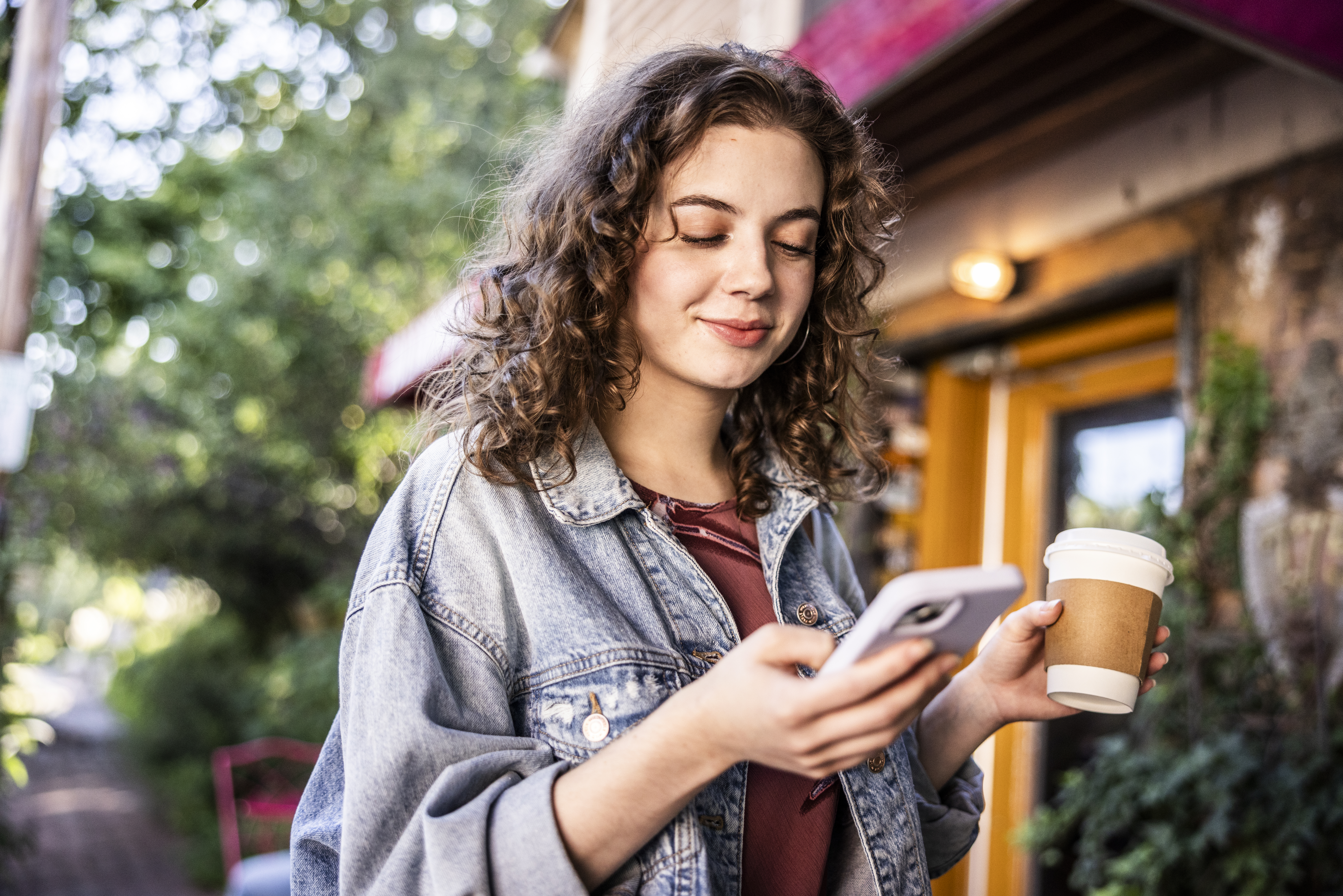 Woman looking down at her phone while holding a warm beverage