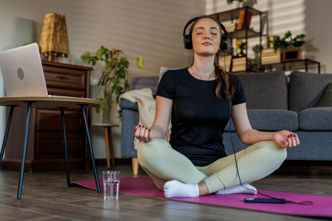 Mujer sentada en una colchoneta de yoga escuchando auriculares mientras medita