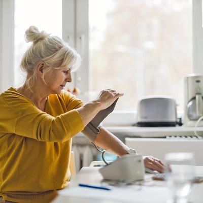 A woman taking her blood pressure in a kitchen